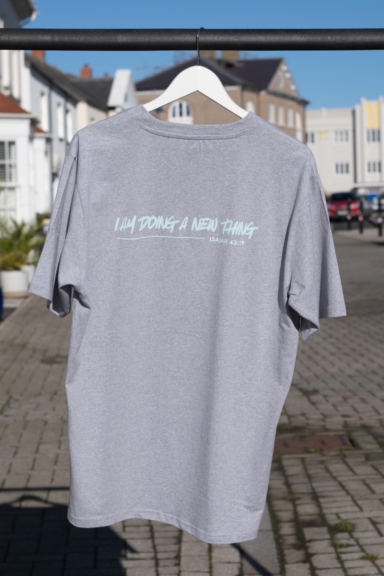 Back of the grey oversized I Am Doing A New Thing T-shirt with the mint script back print and Isaiah 43:19